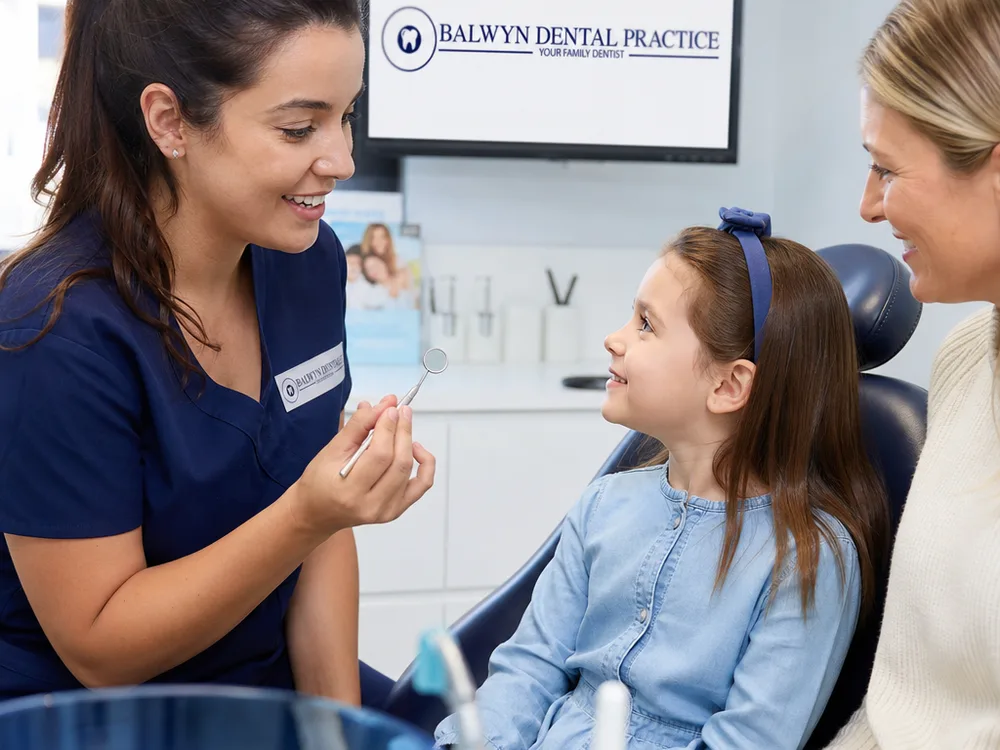 Dentist gently demonstrating a dental mirror to a child with a parent nearby